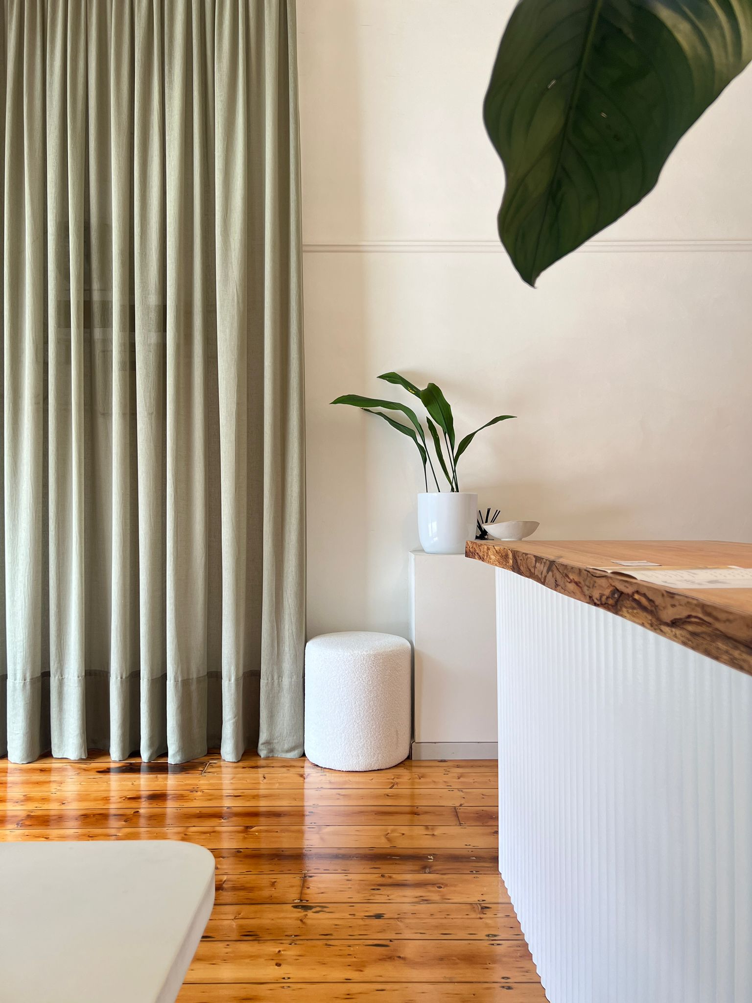 Earlier styling of the reception area with sage-green linen curtains, showing the same counter and material palette in a different colour tone